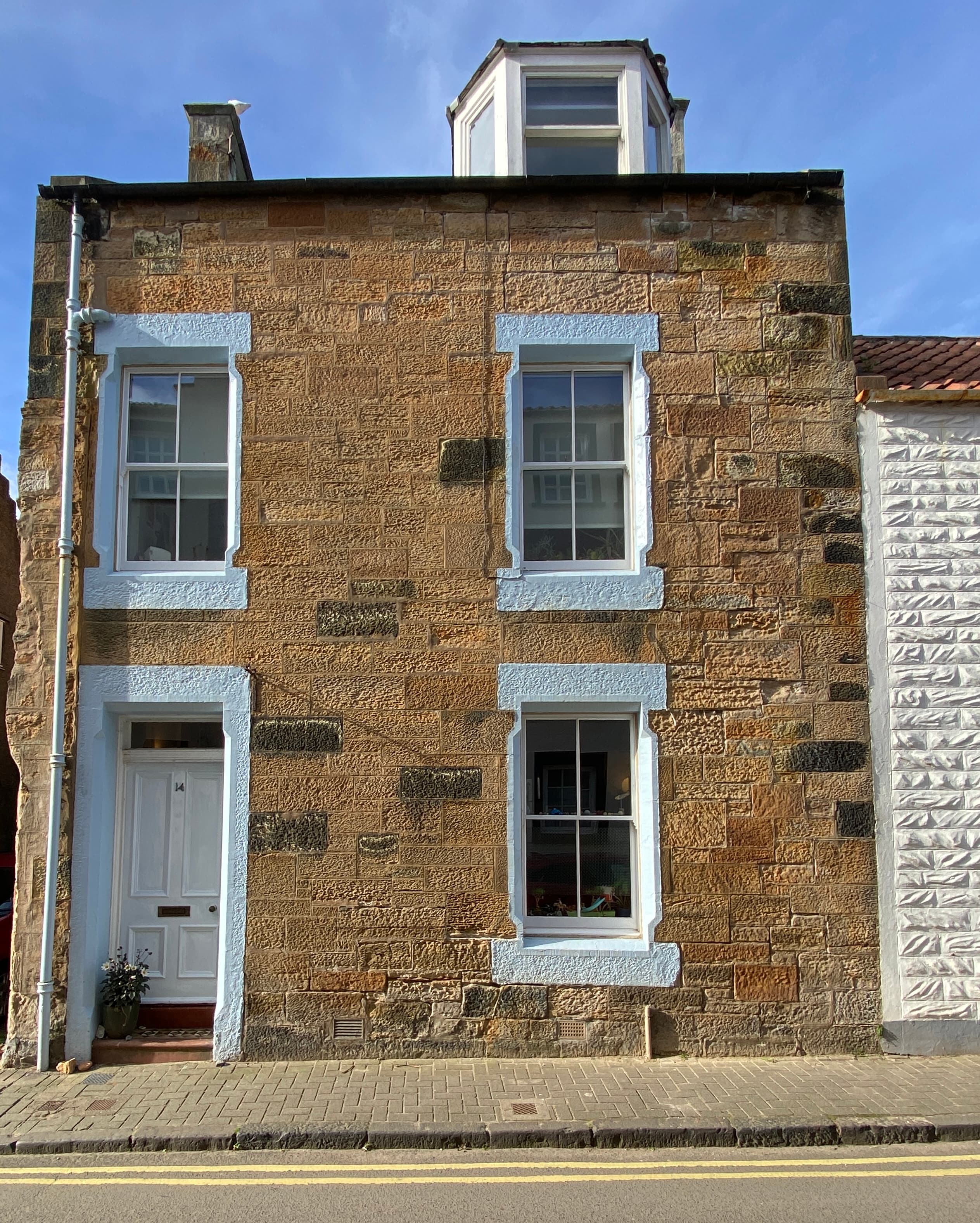 The stone frontage of a waterfront home in Anstruther, with pale blue painted door and window surrounds, white window frames and a roof dormer.