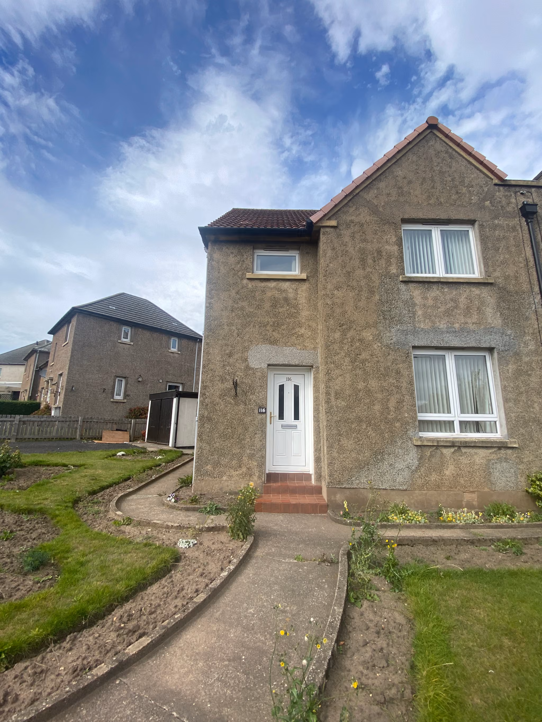 The exterior of Lisa’s home in St Andrews, with a white front door, garden path and rendered frontage beneath a tiled roof.
