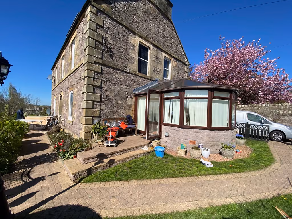 The exterior of Michelle’s stone house in Cupar, with a conservatory, garden path and pink blossom tree.
