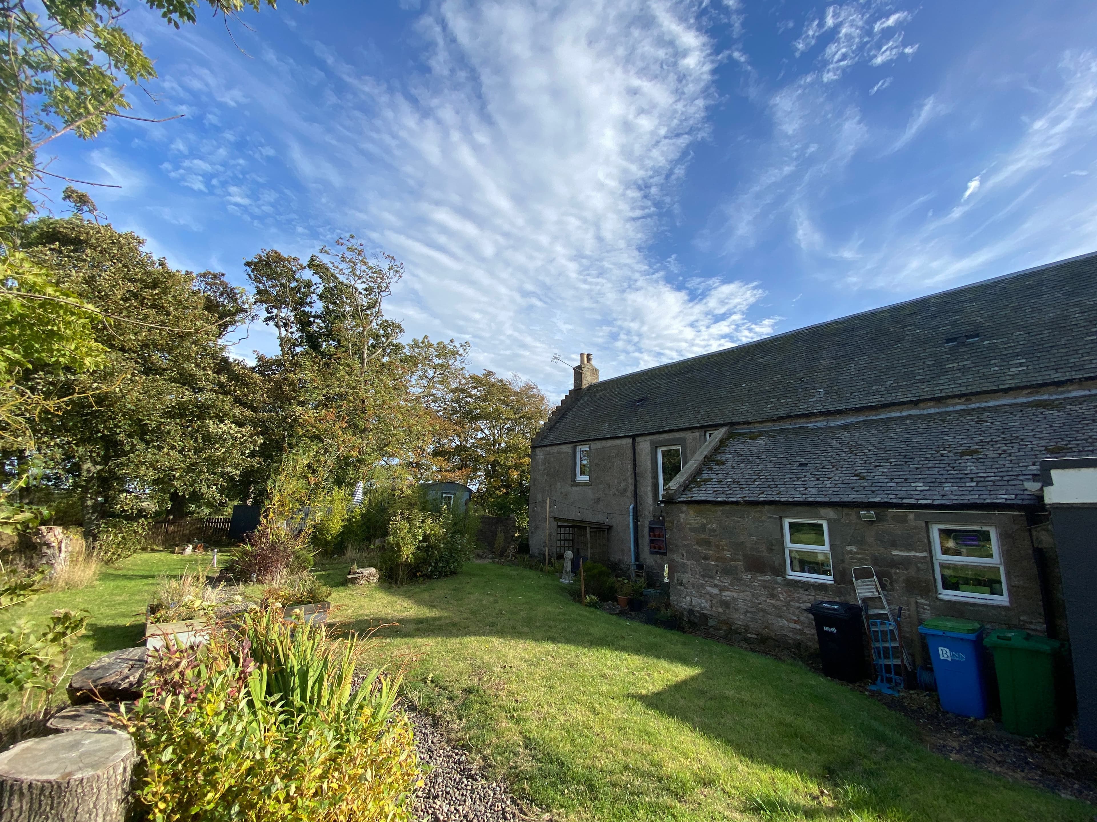 The main stone house in Fife, showing white window frames, painted exterior details and the planted garden.